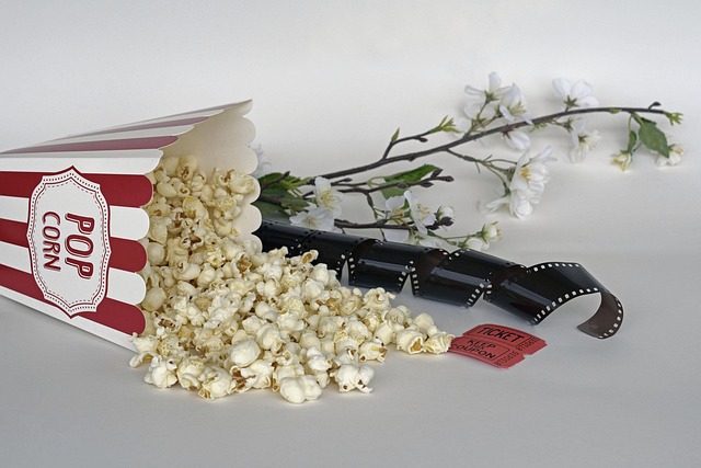 Popcorn, vintage film reel, and classic movie tickets on a wooden surface.